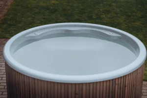 Round fiberglass hot tub filled with clean water, featuring a 3D Granite shell finish and integrated seats, installed outdoors on a brick patio.
