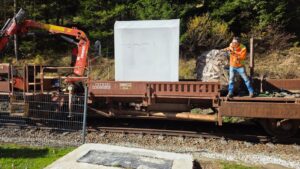 Packaged 2M Cube Sauna on a railway wagon during delivery, with lifting equipment and an unloading crew. 