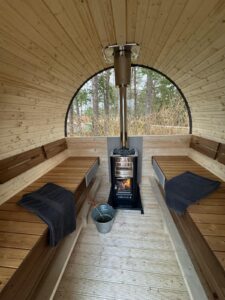 Interior of a 3 m Barrel sauna with a Harvia wood-burning heater, side benches and a half-moon window.