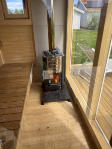 Box sauna interior with a Harvia M3 wood-burning heater and chimney passing through the roof.